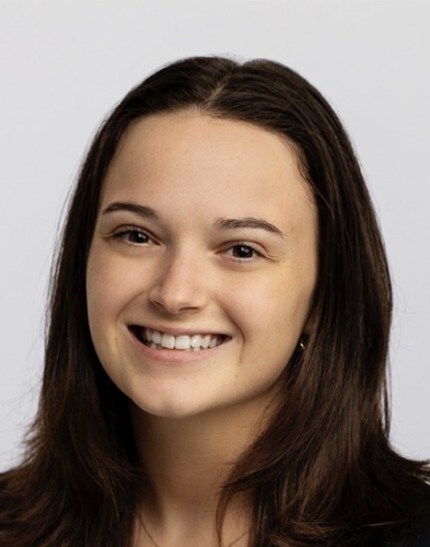 A person with long brown hair and a black shirt smiles against a plain white background.